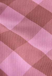 Tissu en textile présentant un motif à carreaux dans des teintes de rose et de marron, avec une texture lisse et des détails tissés visibles.