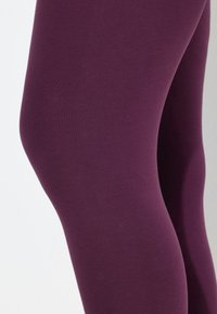 Leggings ceñidos y elásticos en un rico color ciruela, confeccionados con una tela suave y opaca, con un diseño sin costuras y sin patrones o acentos visibles.