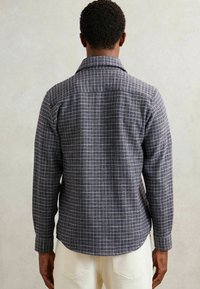 Cămașă gri cu carouri, cu o textură moale, având un guler clasic și mâneci lungi, văzută din spate pe un fundal neutru.