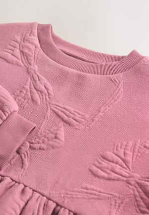 Roze gebreide trui met getextureerde bloemmotieven, een geribde ronde halslijn en geplooide stofaccenten aan de zoom en mouwen.