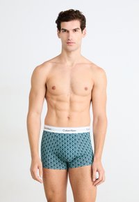 Calvin Klein herenen boxershorts in een teal geometrisch patroon. Voorzien van een witte elastische tailleband met merklogo. Zachte, rekbare stof.