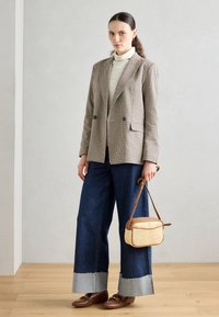 Blazer doppiopetto con motivo houndstooth, dolcevita color crema, jeans in denim scuro a gamba larga con orli grezzi, e una borsa a tracolla marrone. Mocassini marroni completano il look.