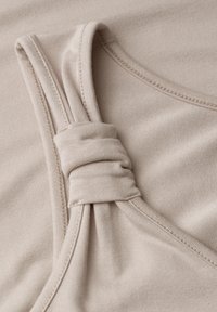Beige ribbed fabric with stitched edges, featuring a gathered knot detail on a garment strap or neckline.