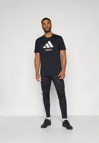 Čierne bavlnené tričko s veľkým bielym logom Adidas a nápisom "JUVENTUS" ružovej farby. Dopĺňané čiernymi nohavicami s bielymi pruhmi.