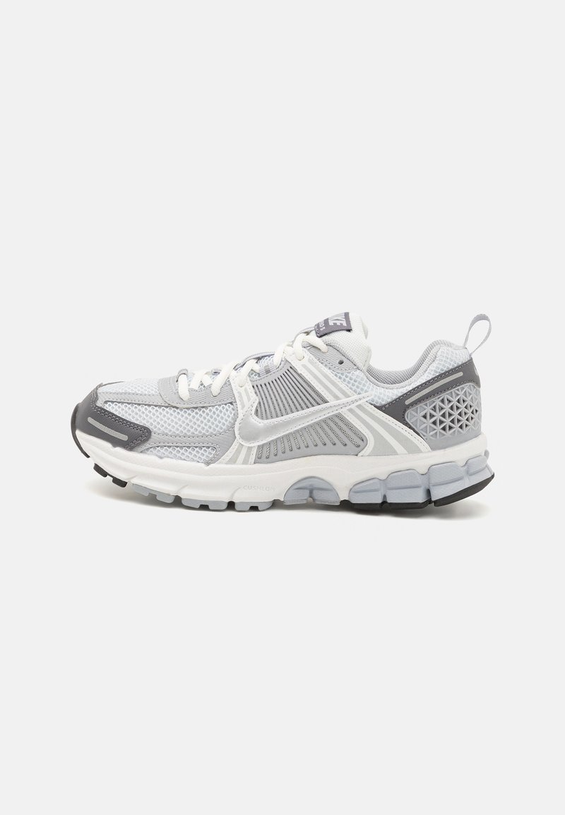 Baskets de sport grises et blanches, fabriquées en matériaux mesh et synthétiques, avec une semelle rembourrée et des accents géométriques sur le talon.