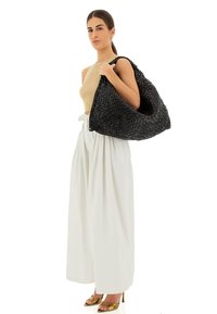 Borsa nera intrecciata a forma di hobo, con superficie testurizzata, ampia apertura e manico robusto. Il modello indossa una maglietta beige e pantaloni bianchi.