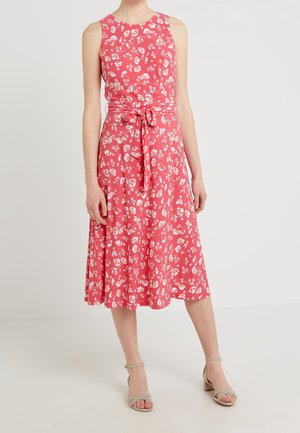 Bezrękawnikowa koralowa sukienka midi z białym kwiatowym wzorem, zawiązywanym paskiem w talii, noszona z beżowymi sandałami na obcasie z paskiem wokół kostki.