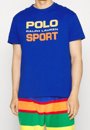 Blaues Baumwoll-T-Shirt mit dem Aufdruck "POLO RALPH LAUREN SPORT" in Gelb und Orange. Kurze Ärmel, runder Halsausschnitt. Kombiniert mit bunten, gestreiften Shorts.