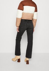 Kurtka puchowa w kolorze brązowym, kremowym i beżowym; w połączeniu z czarnymi jeansami o wysokim stanem i beżowymi butami na słupku.