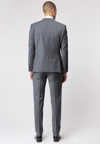 Grau Anzug mit maßgeschneidertem Design, einem einzelnen Schlitz im Rücken, gerade geschnittenen Hosen und eleganten schwarzen Dressschuhen.