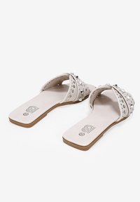 Sandali piatti realizzati in morbido materiale, con una tomaia bianca decorata con borchie e strass argentati. Suola marrone chiaro con logo.