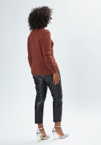 Maglione a maglia color creta, pantaloni in pelle nera a gamba affusolata e scarpe con tacco alto argentate. Tessuto morbido con dettagli luccicanti sulle scarpe.