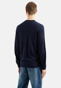 Laivastonsininen neulepusero, jossa on pyöreä pääntie ja pitkät hihat, nähtynä takaa, yhdistettynä vaaleansinisiin farkkuihin. Sileä pinta.