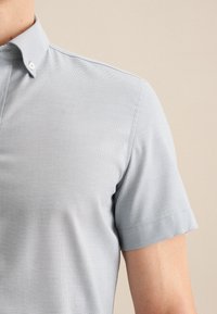 Camicia azzurra chiara a maniche corte con tessuto testurizzato, colletto button-down e vestibilità slim. Dettagli delle cuciture visibili sulle maniche.
