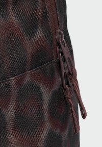 Mochila de tela con patrón oscuro y acabado brillante, con cremalleras marrones contrastantes y cordones para facilitar su apertura, destacando la textura y el diseño.