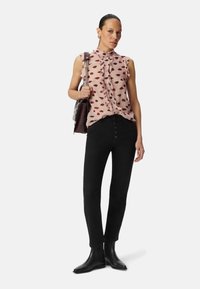Roze top met rode lippenstempel, gerimpelde kraag en knoopsluiting; gecombineerd met high-waisted zwarte jeans en zwarte enkellaarsjes.