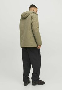 Doudoune verte olive avec capuche, présentant une texture lisse et une coupe légèrement oversize, associée à un pantalon cargo noir et des bottes noires.