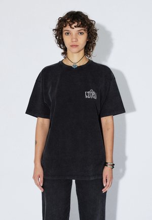 Zwart oversized katoenen T-shirt met ronde hals, korte mouwen en een voorkant met de tekst "UTOPIA". Zacht, licht gestructureerd materiaal.