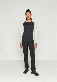 Black long-sleeve top with light gray sleeves, featuring a logo on the chest. Paired with black pants and black shoes, standing against a plain background.