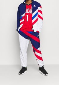 Red jersey with "1" and NBA logo, blue and white jacket with diagonal red stripes, matching pants, black athletic shoes.