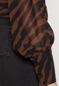 Blusa rigata marrone e nera trasparente con maniche a palloncino e polsini abbottonati, abbinata a una gonna nera strutturata.