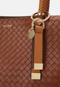 Bruine geweven leren handtas met een goudkleurige ring en accenten, voorzien van een goudkleurig logo-label en gestructureerde details.