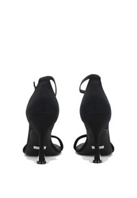Sandalias de tacón negro con una textura similar al ante, con la parte trasera abierta y tiras delgadas en el tobillo. Presentan un elegante tacón de aguja y una silueta curva.