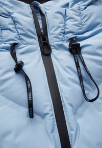 Ljusblå puffjacka med dragkedja fram, svart dragkedja och snörning, strukturerad tyg och vadderad quilt-design.