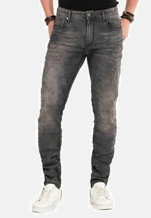 Jean en denim gris à coupe slim, avec une texture délavée, des poches avant et une fermeture à bouton. Porté avec des baskets blanches.