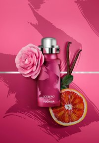 Fuchsia-flaska med ett silverlock, omgiven av en rosa ros, vaniljstänger och en skivad blodapelsin på en rosa bakgrund.