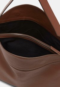 Brown leather tote bag with a textured finish, featuring a black interior and a zippered compartment for secure storage.