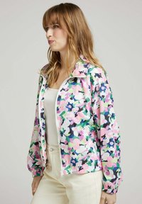 Veste légère à motif floral, présentant des teintes pastel de rose, vert et bleu, avec une fermeture éclair à l'avant et des poignets élastiques.