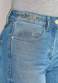 Spijkerbroeken met een hoge taille, lichtblauwe kleur, gouden hardware accenten en zichtbare stiksels. Beschikt over meerdere zakken.