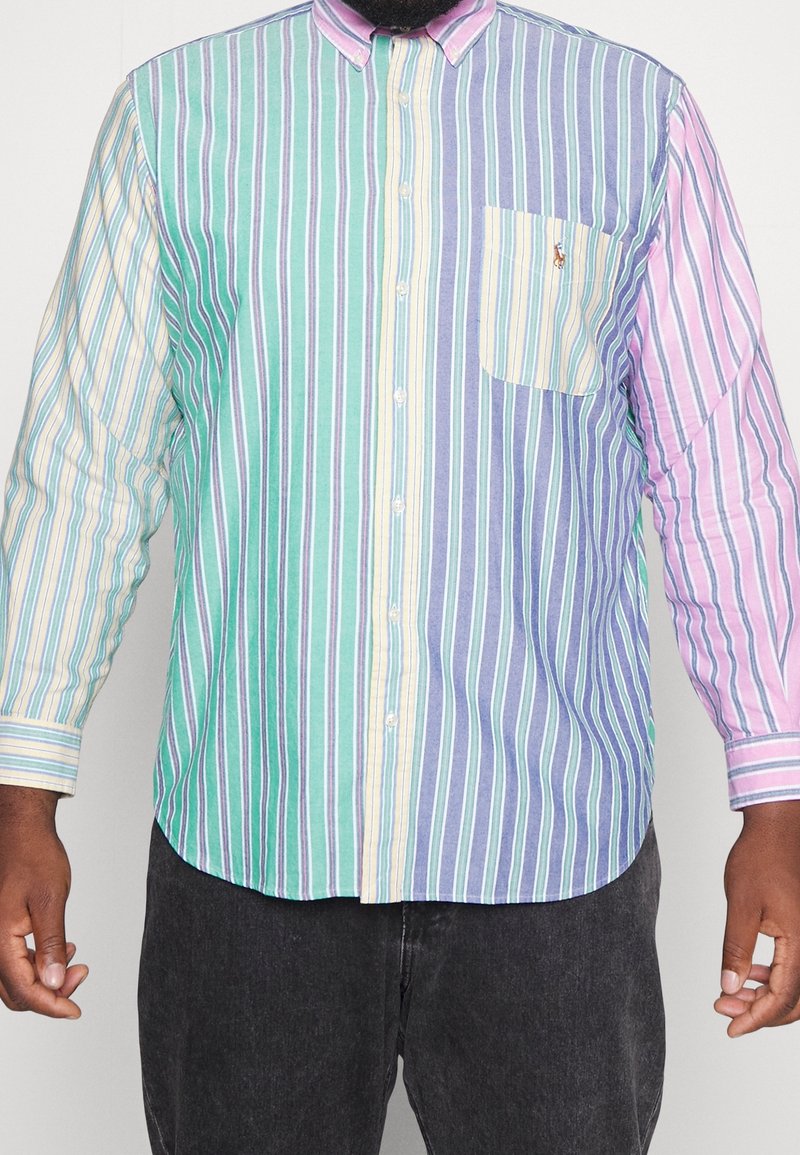 Camisa abotonada con rayas de colores que incluyen verde, azul, rosa y amarillo. Cuenta con un bolsillo en el pecho frontal y un diseño de cuello distintivo.