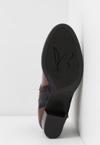 Chaussure en daim marron et bleu marine avec une semelle en caoutchouc noir texturée. Dotée d'un logo papillon et d'accents décoratifs en métal sur le côté.