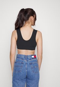 Mörkgrå, ribbade crop top med breda axelremmar, kombinerad med högmidjade, blå denimjeans som har ett logopatch på baksidan.