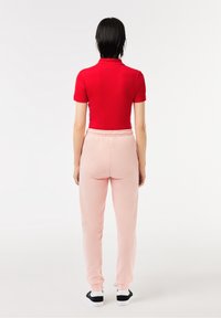 Camisa polo roja de manga corta con cuello alto, combinada con pantalones de chándal rosa claro que tienen una cinturilla elástica y dobladillos acampanados.