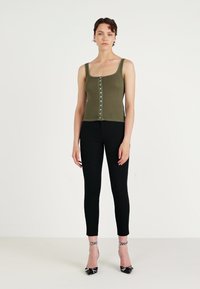 Olive green ribbed tank top with square neckline, front button closure, paired with black skinny pants and black and white checkered heels.