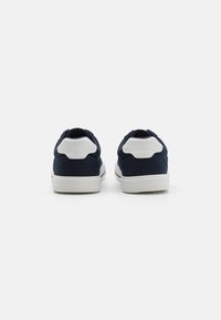 Navy canvas sneakers with white synthetic accents, featuring a textured sole, padded collar, and rounded toe, viewed from the back.