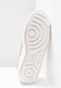 Sneaker Nike con suola in gomma bianca caratterizzata da motivi circolari. La tomaia è in morbida pelle scamosciata rosa chiaro. Vista dal basso mostra il disegno dettagliato del battistrada.