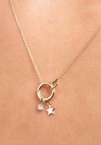 Delicate gold chain necklace with a round pendant featuring a small star charm and a sparkling clear gemstone charm.