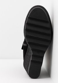 Svart sko med en strukturerad yta och kraftig gummisula som har horisontella spår för grepp. Synlig kardborreband på sidan.