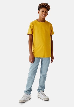 Gelbes Baumwoll-T-Shirt mit kurzen Ärmeln, kombiniert mit hellblauen Jeans und weißen Sneakern. Einfaches Design und lässige Passform.