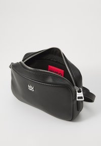 Black leather bag with a textured surface, silver hardware, zip closure, and red interior label. Compact design with a single strap.
