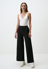 Body bianco a coste con scollo a V abbinato a pantaloni neri a gamba larga in maglia testurizzata e sneakers bianche.