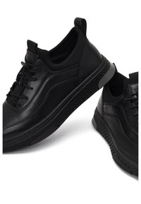 Zapatillas negras de cuero liso, con suela de goma texturizada, punta redondeada y cordones, con un cuello acolchado y tira de agarre.