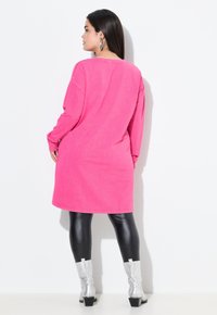 Abito rosa a maniche lunghe con una vestibilità ampia, caratterizzato da un collo rotondo. Abbinato a stivali argento lucidi al ginocchio e leggings neri.