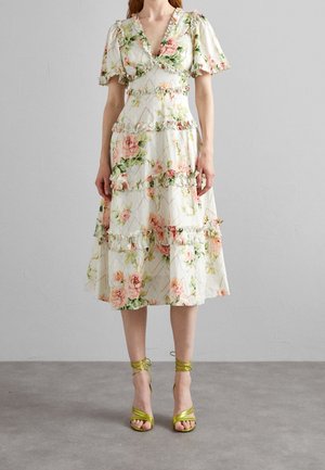 Blomstret kjole med korte pufærmer, flæsekant og lagdelt design. Har en hvid base med pink og grønne blomster. Bruges med grønne høje hæle.