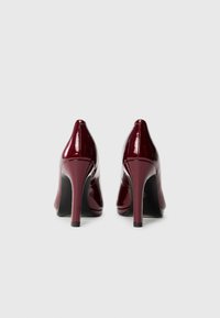 Escarpins en vernis bourgogne avec des pointes et des talons aiguilles. Texture lisse avec des accents minimes et un design élégant et épuré.