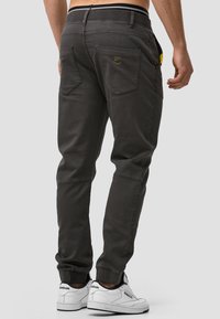 Pantalones cargo gris oscuro con puños elásticos en los tobillos, bolsillos traseros y acentos amarillos. Fabricados en una tela de textura suave y con costuras reforzadas.